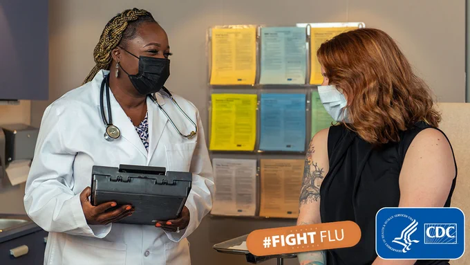 Health care provider and patient smile while having a conversation in a clinical setting. In the bottom right hand corner is the #FightFlu logo next to the CDC/HHS logo.  