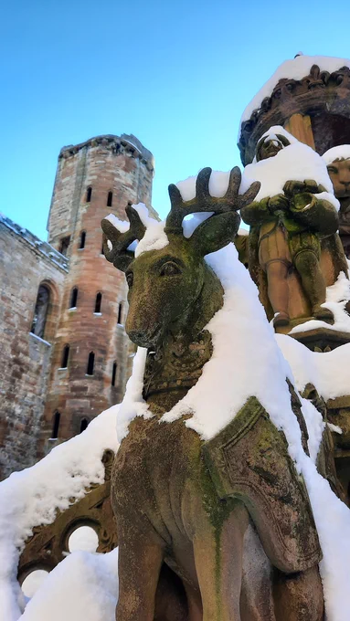 Snow on top of a carving of a stag on a historic stone fountain in a palace courtyard.