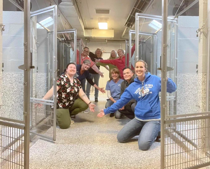 several shelter volunteers crowd a hallway with their arms raised in excitement. all the kennel doors are swung open around them, showing there are no animals left in the building