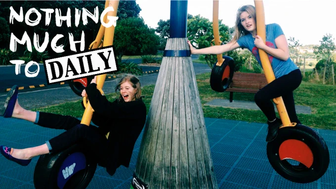 Image of Beatrice and Hero from NMTD on an octopus swing. Beatrice leans back on her tire on the left, while Hero leans against the main pole on the right. Text above Bea's head reads: Nothing Much To Daily. Photo taken by Sally Bollinger, 2014