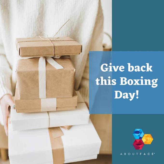 photo of a person holding a stack of boxes with ribbons. White text on the right reads "Give back this Boxing Day". The AboutFace logo is in the bottom right corner. 