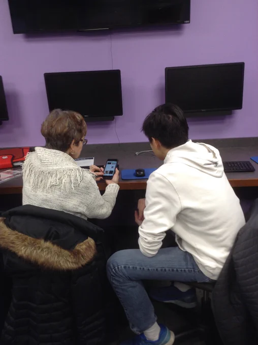 Women holding and looking at cell phone with teenager in library technology center.