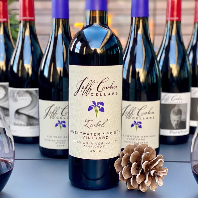 Bottles of Jeff Cohn Cellars wines on a fire pit table with glasses and a pinecone.