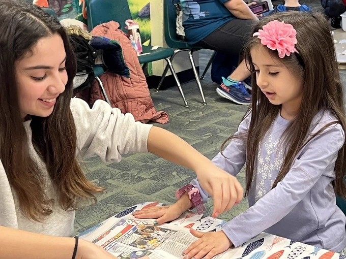 Teen helping child with craft at the library
