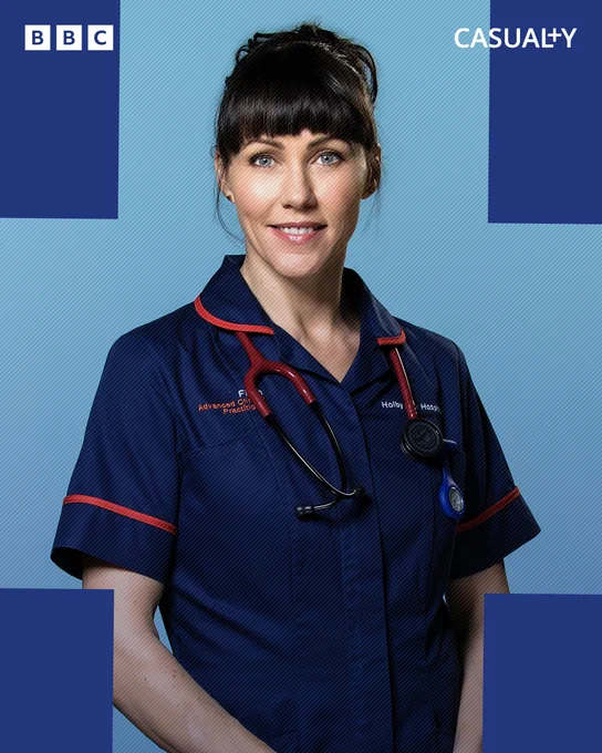 Faith Cadogan (Kirsty Mitchell) wears navy scrubs and a stethoscope around her neck. She smiles at the camera. 