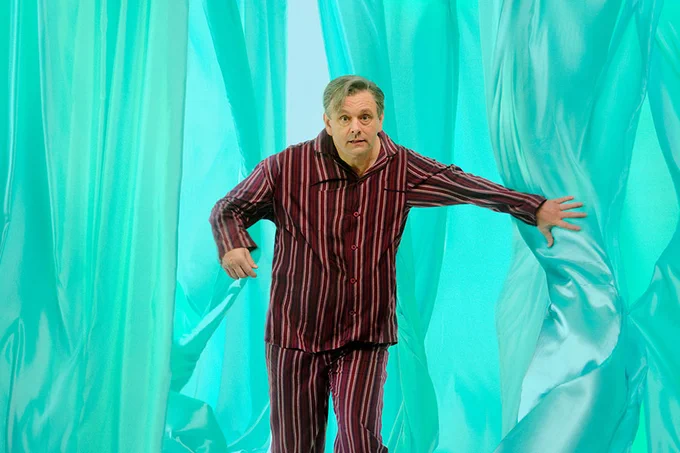A photo showing a man in pyjamas leaning against a pale blue backdrop