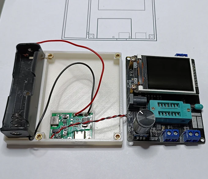 A 18650 battery holder connected to a small charger PCB, connected to a more complex module (a component tested) all roughly placed on top of a white 3D-printed plastic base.