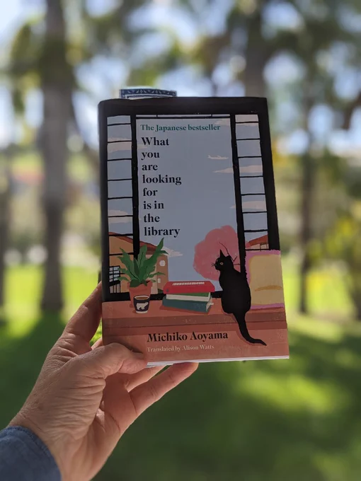 Copy of a hand holding a book :  "What you are looking for us in the library" by Michiko Aoyama