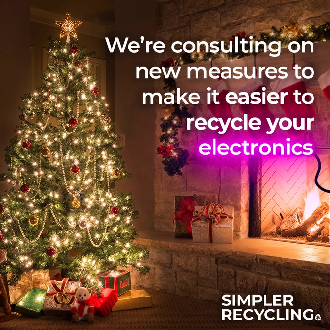 A bright lit up Christmas tree in front of a cozy fireplace, it has the text saying 'we're consulting on new measures to make it easier to recycle your electronics' - the word electronics is written in pink neon text