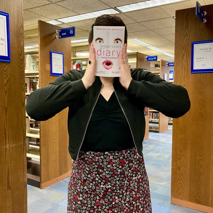 Bookface picture posed with cover of Bridget Jones Diary standing in the aisles at the library