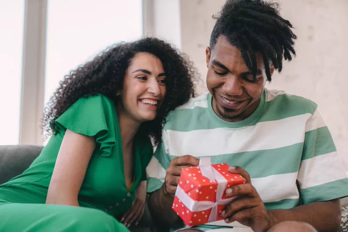 Woman gives her significant other a gift while the couple cuddles on a couch