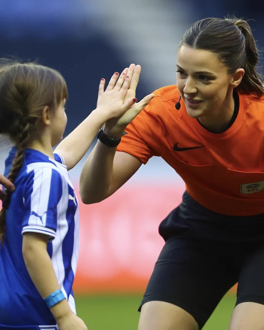 Assistant referee Emily Carney giving a high five to a Wigan Athletic mascot.