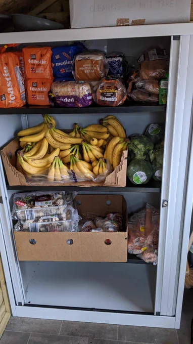 A community larder showing the shelves full of bananas, mushrooms, bread, carrots and broccoli.