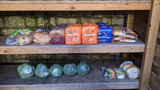 A community larder with wooden shelves of donated bread and broccoli.