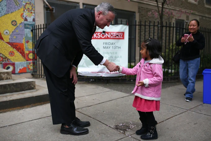 Mayor Jim Kenney leaning over to shake hands with a small child outside of a school.