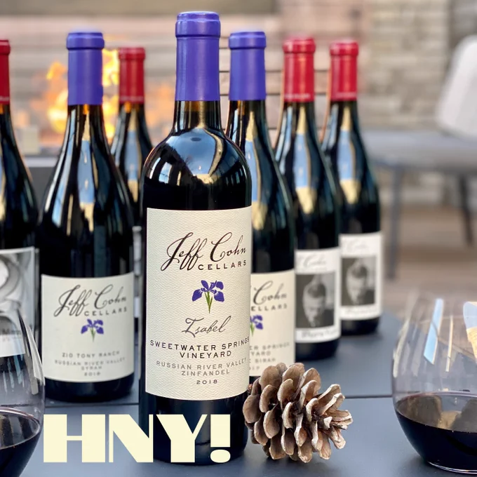 Bottles of Jeff Cohn Cellars wine on an outdoor table with 2 glasses and a pinecone.