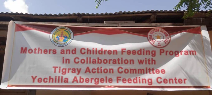 A white banner with red lettering that reads "Mothers and Children Feeding Program In Collaboration with Tigray Action Committee Yechilla Abergele Feeding Center" 