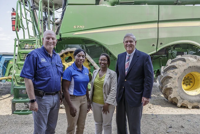 USDA Secretary Tom Vilsack poses with farmers in Arkansas in front of a large piece of farming machinery. 