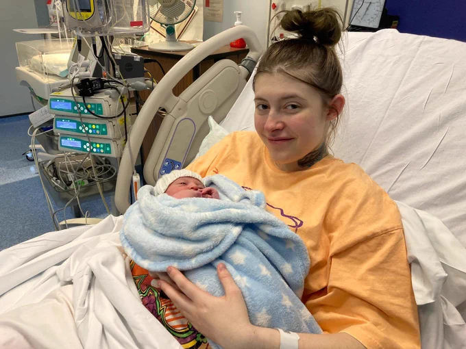 A young woman lays in a hospital bed holding a newborn baby