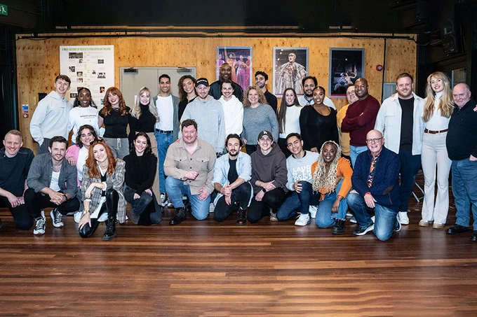  photo showing a group of individuals aseembled in a rehearsal room, smiling at the camera