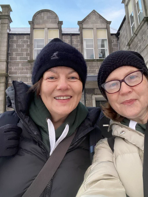 Selfie of two women outside an old building - they are wrapped up warm with hats and coats