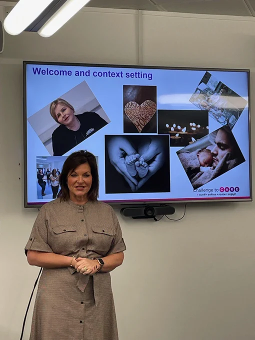 North West NHS Regional Chief Midwife Claire Mathews introduces the context for the workshop standing in front of a large screen depicting images of the many varied aspects of midwifery roles
