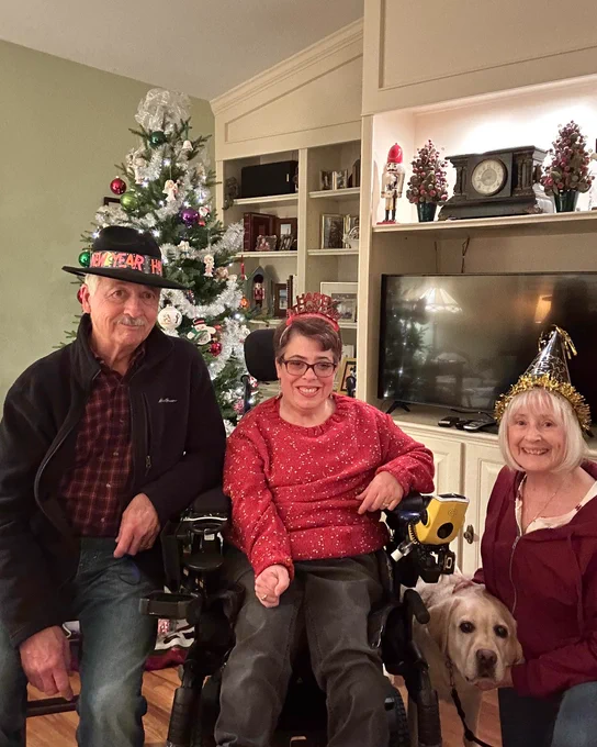 Photo of a family in front of a Christmas tree everyone is dressed in festive gear and smiling.