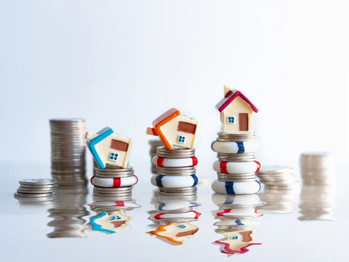 Mini houses surrounded by water, sitting on stacks of coins.