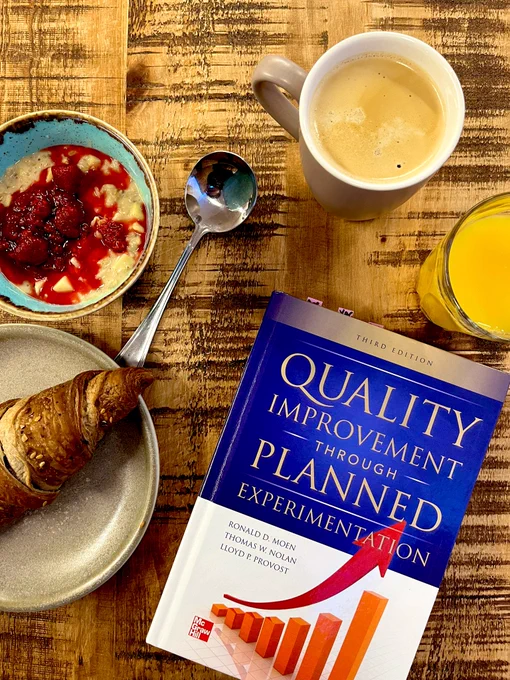Photo of a book titled Quality Improvement Through Planned Experimentation. The book is surrounded by a croissant, porridge with berry coulis, coffee and orange juice