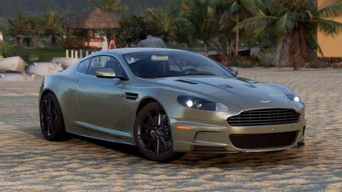 A 2008 Aston Martin DBS finished in my interpretation of California Sage parked on the beach in front of the Lugar Tranquillo Player House in Forza Horizon 5.