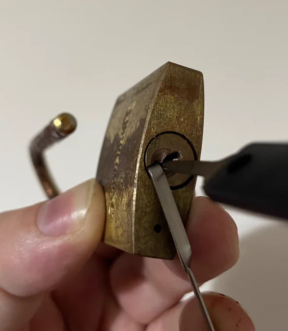 A brass padlock opened with lock picking tools.