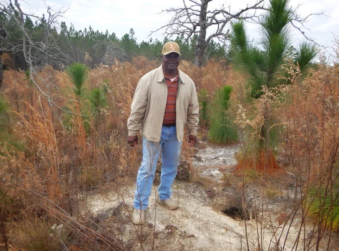 Herbert Hodges stands in front of young longleaf pine trees and next to a gopher tortoise hole. Photo by NRCS Georgia.
