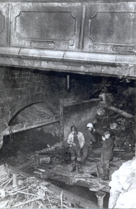 Black and white photo of three work men standing in what could be a sewer or a culvert, or flood outlet, or under a bridge - we don't know - yet...