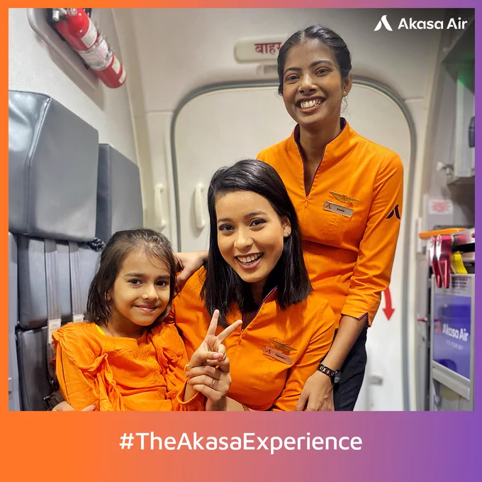Happy young passenger dressed in orange, on an Akasa Air flight with the Cabin Crew