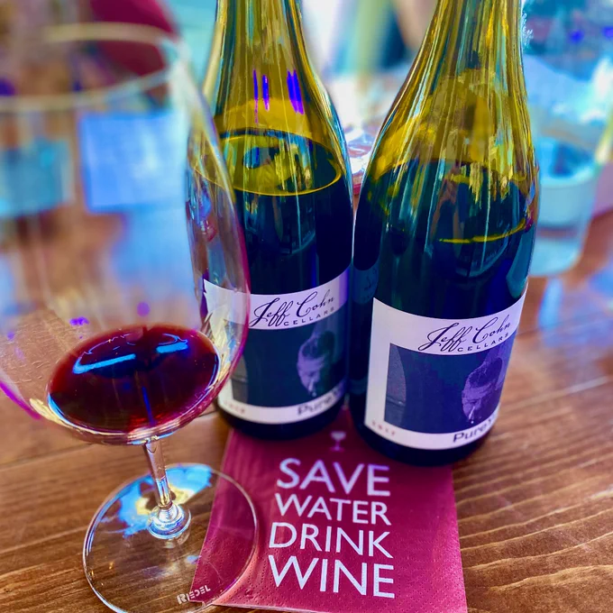 Two bottles of Jeff Cohn Cellars Pure Yum on table in the tasting room with a glass and napkin that says, " save water, drink wine" .