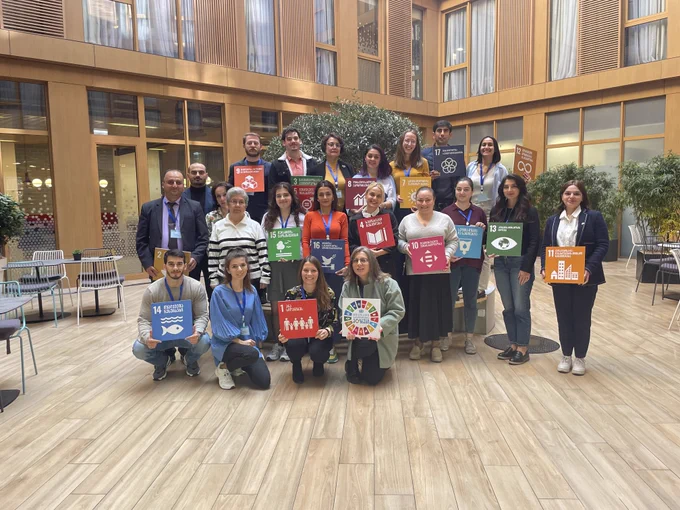 The picture shows a group of around 20 people, who are taking a group picture. In their hands, they have icons that represent the Sustainable Development Goals.