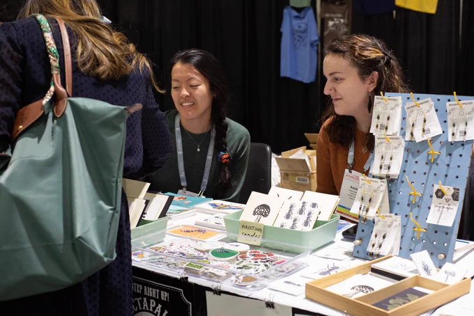 Two graduate students sitting behind a table with insect-themed art and jewelry interacting with a visitor.