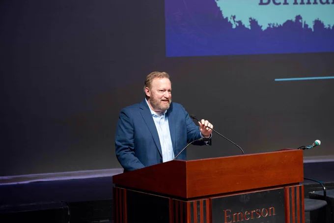A person wearing a blue blazer speaks at a podium with the word "Emerson" on it.