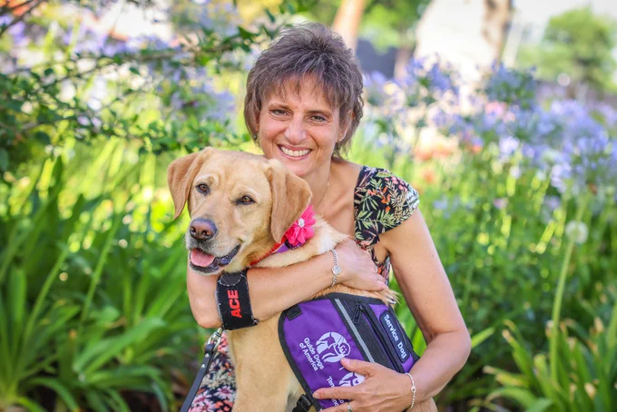 In this photo, a woman hugs her yellow Lab service dog.