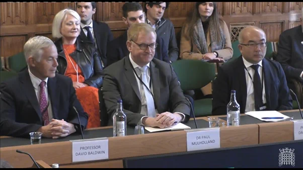 Group of people sitting at table in front of microphones.