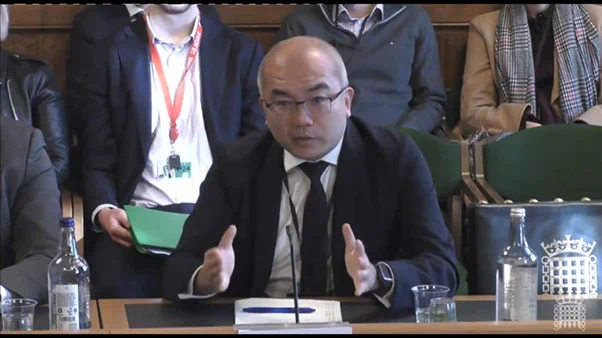 Prof David Chang sitting at table in front of microphone in suit and tie.