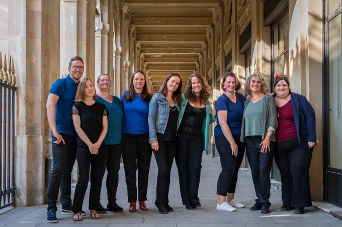 photo de l'équipe Trilogue (presque) au complet : Ludovic, Marina, Sandrine, Charline, Périne, Florine, Mathilde, Julie et Morgane en tenue décontractée, souriants, dans un décor architectural ancien. 