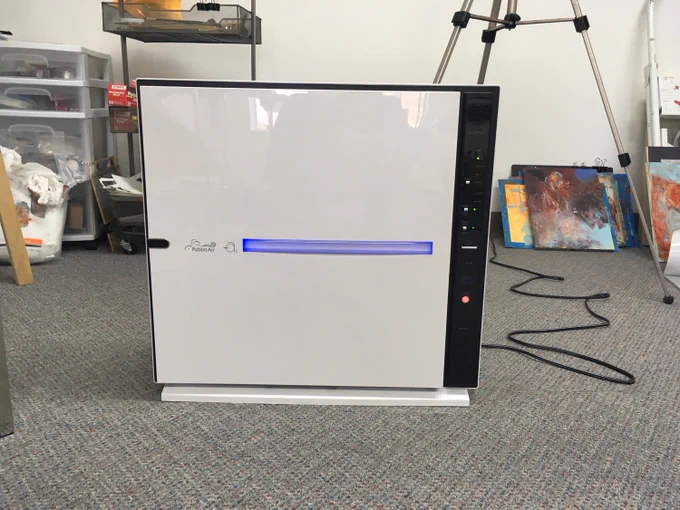 A MinusA2 air purifier with a simple white front panel stands in an artist's studio, surrounded by colorful paintings and creative supplies