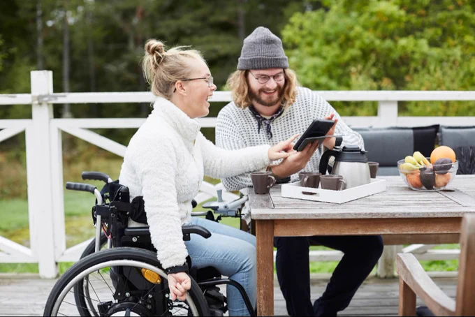 Person with cerebral palsy and their caregiver drinking coffee at an outdoor picnic table.
