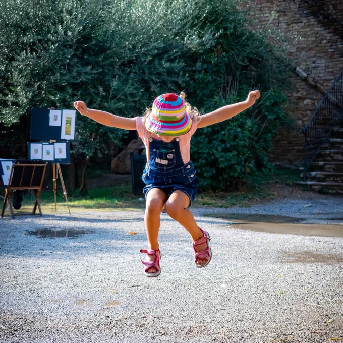 Child wearing brightly coloured stripy hat jumping with arms extended
