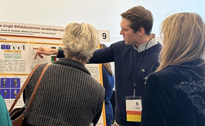 A man points at a research poster as two women look on.