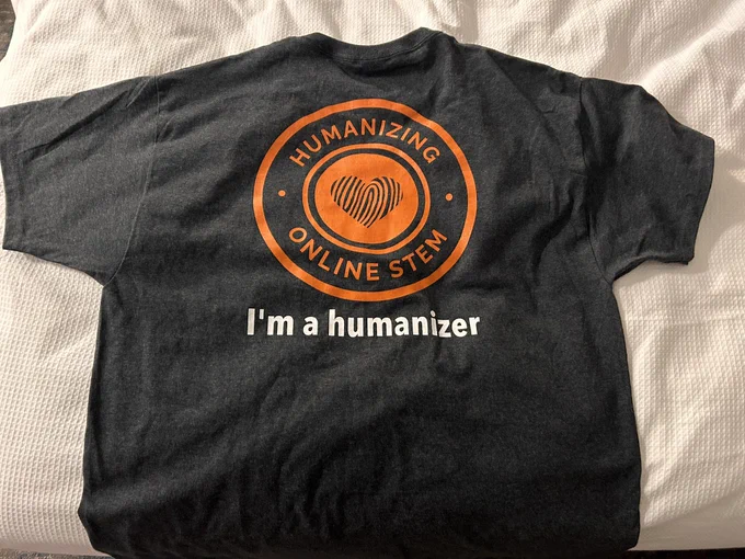 A t shirt that says, “I’m a humanizer!” In the center is a heart shaped fingerprint and Humanizing Online STEM.