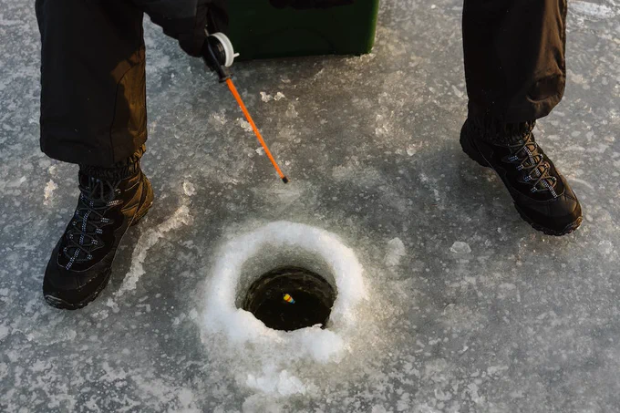 A view looking down at someone sitting down ice fishing. 