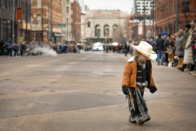 A kid wearing cowboy attire walking in downtown Denver.