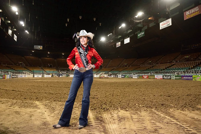 A rodeo queen in a bedazzled cowboy hat, red Western shirt, boots, a belt buckle and a sash that says Miss Rodeo Colorado.